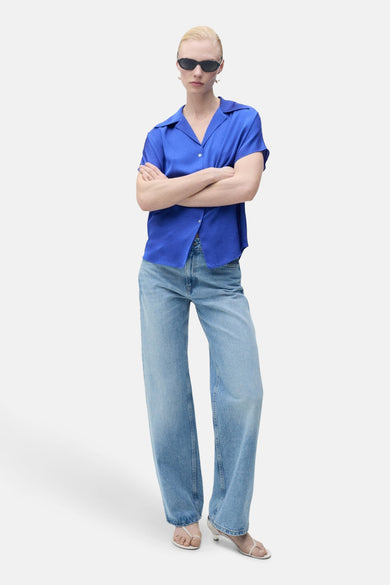 Chemise bleue à manches courtes de MANGO, portée avec un jean décontracté et des sandales blanches.