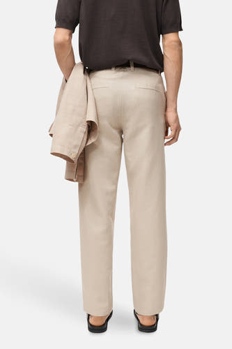 Pantalon écru de MANGO, vu de l'arrière avec un chemisier brun et une veste coordonnée en main.