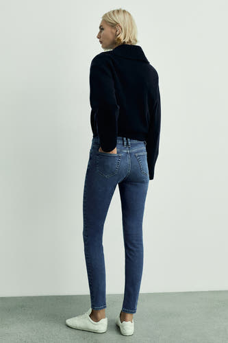 Jean skinny en denim mid-blue de MANGO, vu vu de l'arrière, associé à une veste bleu marine et des baskets blanches.