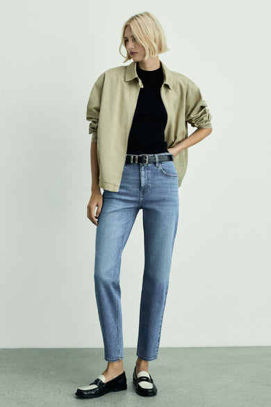 Jean mom bleu mid de MANGO, porté avec un haut noir, une veste beige et des loafers noir et blanc.