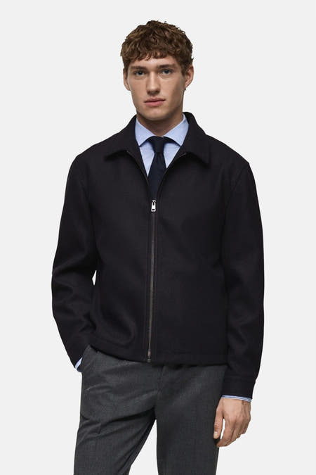 Gilet bleu de MANGO porté sur un chemisier bleu clair avec une cravate bleu foncé et un pantalon gris.