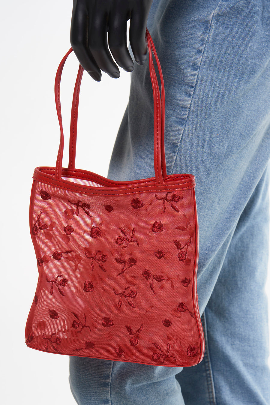 Rode handtas met bloemenpatroon, vastgehouden door een zwarte handschoen, op een blauwe jeans achtergrond.