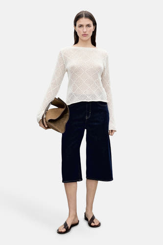 Ecru ronde hals trui van MANGO, met een open gebreide textuur, gecombineerd met donkere denim bermuda en leren sandalen.
