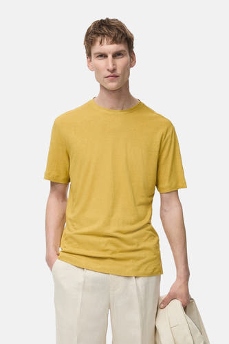 T-shirt jaune à manches courtes de MANGO, porté avec un pantalon beige, en tenant un manteau.