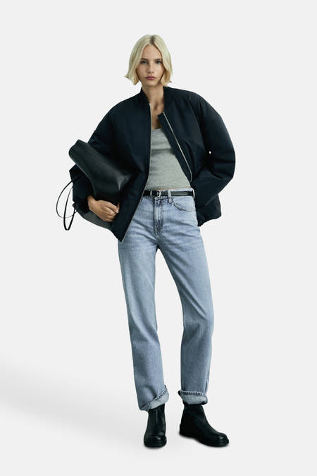 Jean droit bleu clair de MANGO, avec une taille classique et des poches arrière, porté avec un haut gris et des chaussures noires.