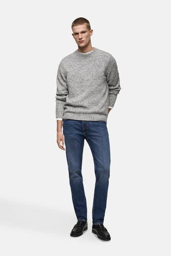 Jean slim de MANGO en denim bleu moyen, porté avec un pull gris et des chaussures noires.