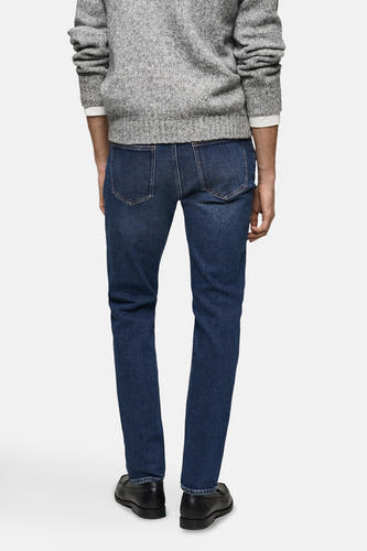Jean slim de MANGO en denim bleu moyen, vu du l'arrière, combiné avec un pull gris et des chaussures noires en cuir.