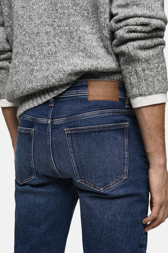 Jean slim fit en denim bleu moyen de MANGO, vue arrière, associé à une chemise grise.