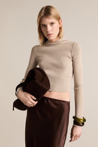 Pull beige à col rond de MANGO, avec des manches longues et des finitions côtelées, porté avec une jupe brune et des bottes.