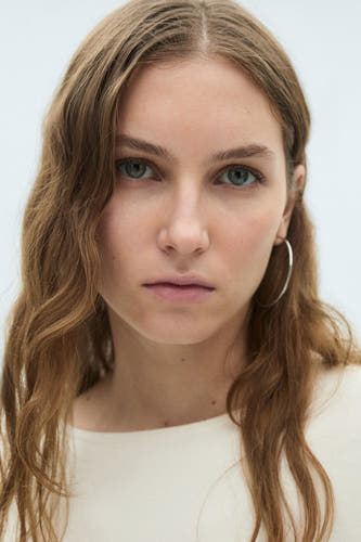 Pull-over blanc à col rond de MANGO, portrait rapproché d'une femme avec une bague d'oreille en argent.