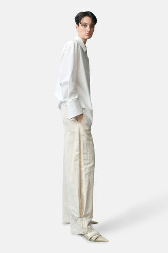 Pantalon écru de MANGO, avec des jambes larges et associé à une chemise blanche et des chaussures pointues.