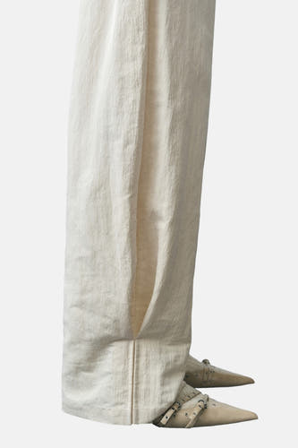 Ecru broek van MANGO, met een wijde pijp en subtiele plooien aan de onderkant, te zien met puntige schoenen.
