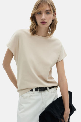 T-shirt beige à manches courtes de MANGO, porté avec des jeans blancs et une sac noir.