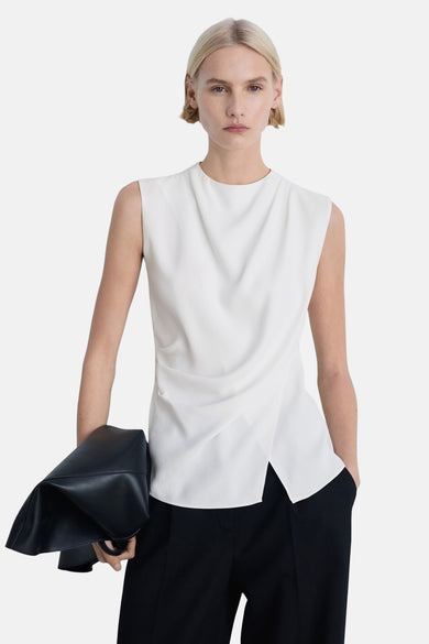 Blouse blanche sans manches de MANGO, avec détail drapé et associée à un pantalon noir.