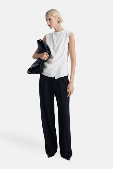 Blouse blanche sans manches de MANGO, portée avec un pantalon noir et une sacoche en cuir noir.