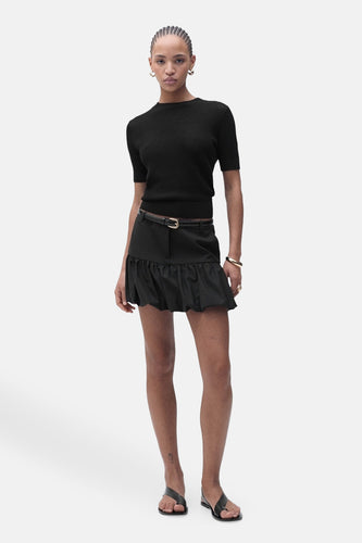 Vrouw in zwarte top en rok, staand.
