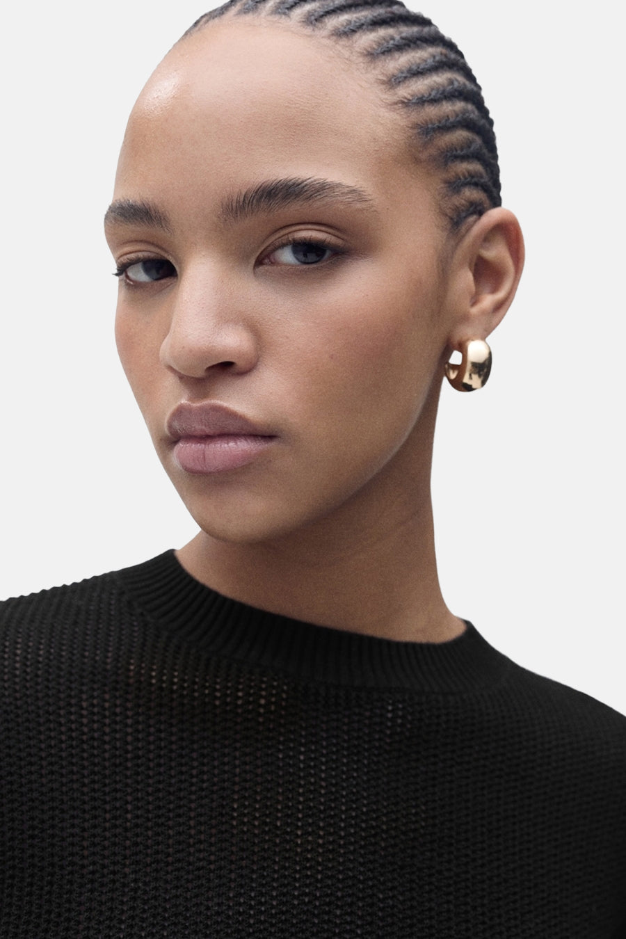 Portret van vrouw met gevlochten haar, gouden oorbellen en zwarte trui.