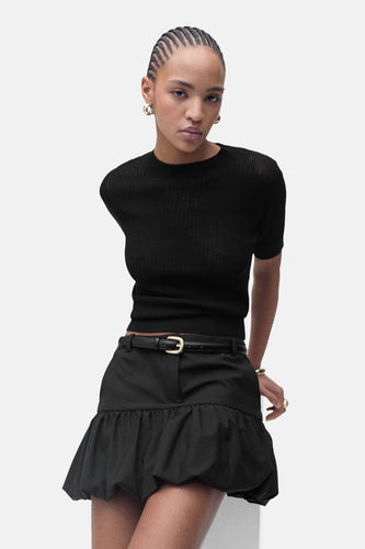 Vrouw in zwarte blouse en rok, staand.
