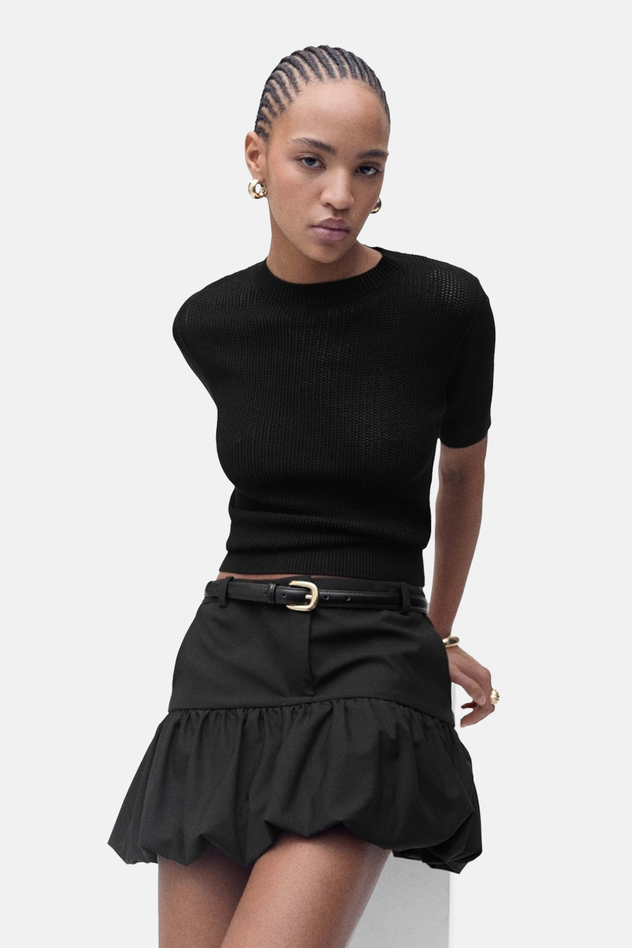 Vrouw in zwarte blouse en rok, staand.
