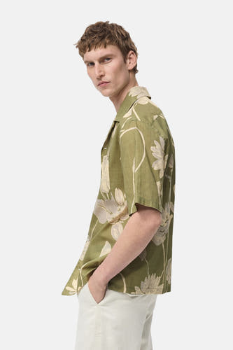 Chemise verte à manches courtes de MANGO, avec un motif floral et portée avec un pantalon blanc.
