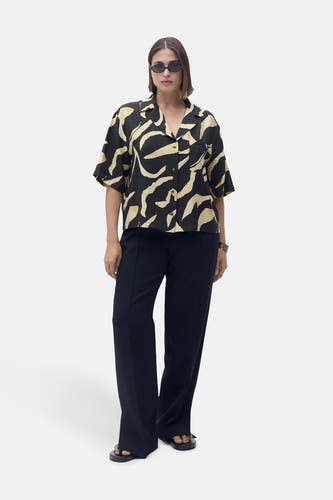 Chemise noire à manches courtes de MANGO, avec un motif abstrait beige, portée avec un pantalon noir et des sandales.