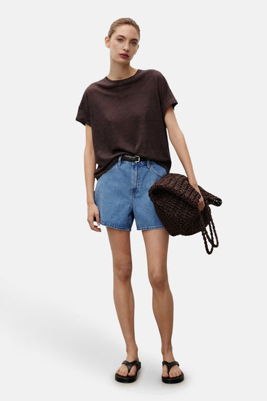 Shorts en denim bleu marine de MANGO, associés à un T-shirt marron, une sac tissé et des pantoufles noires.
