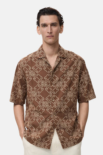 Chemise brune à manches courtes de MANGO, avec un imprimé floral sur toute la surface et une encolure ouverte.