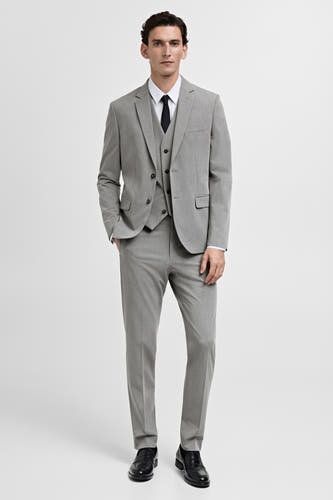 Gilet gris de MANGO, porté sous un costume à carreaux et des chaussures élégantes.