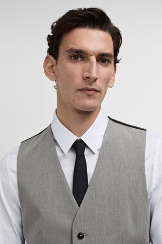 Gilet gris de MANGO, porté sur une chemise blanche avec un nœud papillon noir.
