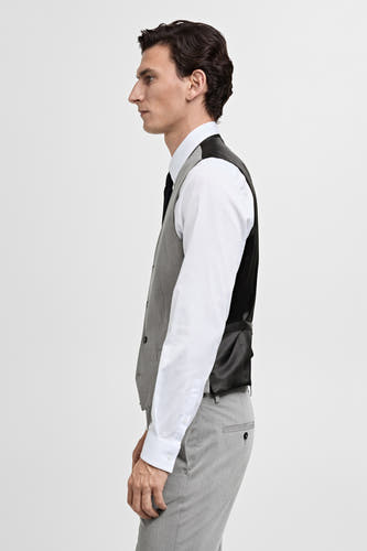 Gilet gris de MANGO, avec un côté avant gris et un dos en satin noir, porté sur une chemise blanche avec une cravate noire et un pantalon gris.