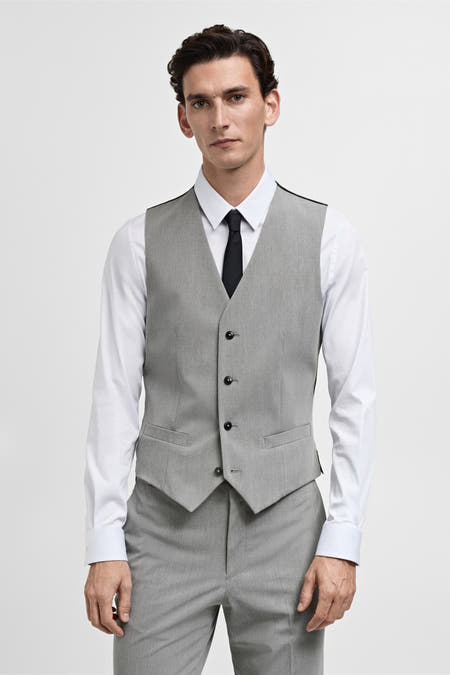 Gilet gris de MANGO porté sur une chemise blanche avec une cravate noire et un pantalon gris.