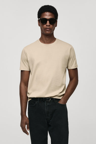 T-shirt beige à manches courtes de MANGO, avec des jeans foncés et un chapeau de soleil.