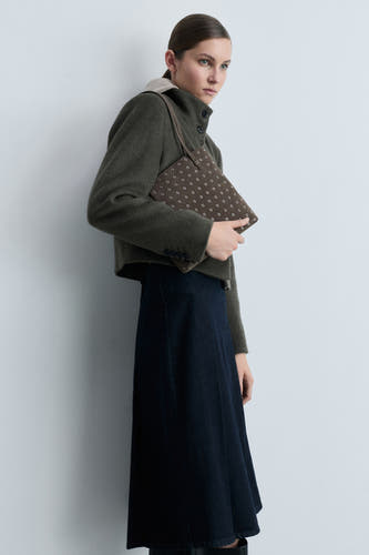 Sac à main marron de MANGO, orné de points blancs contrastants et porté par un modèle en une jupe bleu marine et un blouson vert.