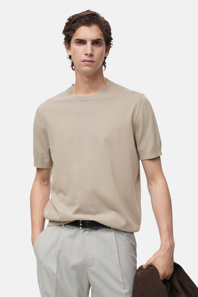 T-shirt beige à manches courtes de MANGO, porté avec un pantalon gris et une ceinture noire.