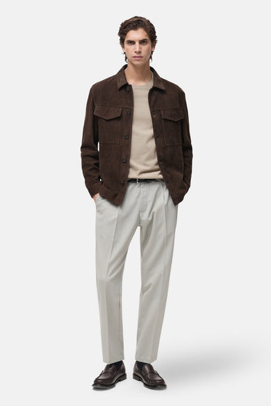 T-shirt beige à manches courtes de MANGO, porté sous un blouson marron avec des pantalons gris clair et des loafers marrons.