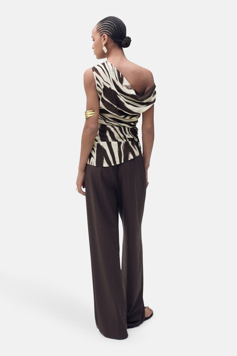 Model van achteren, bruine broek, zebraprint top, gouden armband, opgestoken haar.
