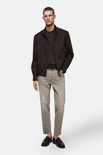 Jean tapered gris MANGO, associé à un manteau brun foncé et des loafers en cuir noirs.
