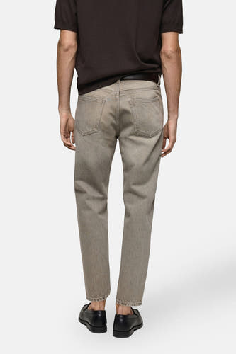 Jean tapered gris MANGO, vu de l'rière avec un un-shirtin et et des chaussures noires.