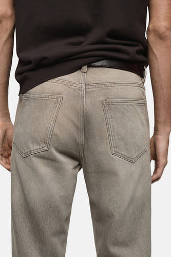 Jean tapered gris MANGO, avec des poches arrière et une ceinture en cuir marron foncé.