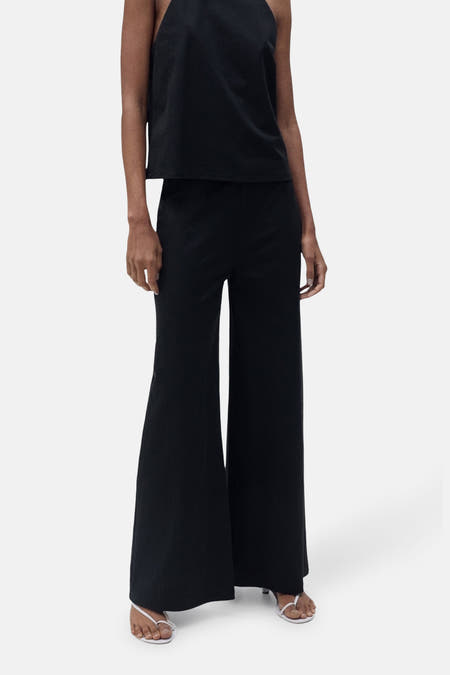 Pantalon noir de MANGO, avec des jambes larges et associé à une chemise sans manches et à des sandales blanches.