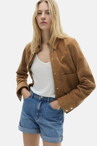 Vrouw met bruine suede jas, wit T-shirt en denim shorts.