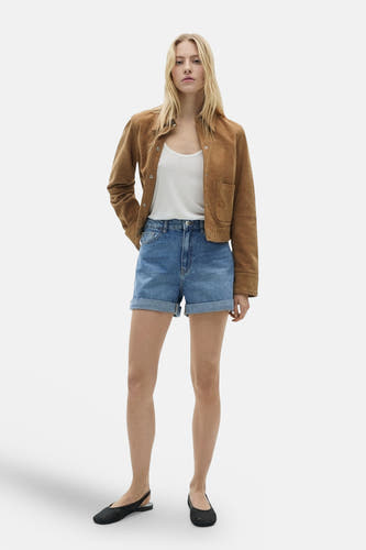 Shorts en denim bleu court de MANGO, associés à un chemisier blanc et une veste marron.