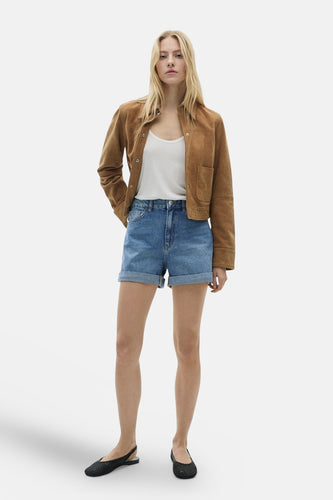 Vrouw in bruine jas, witte top, denim shorts en zwarte schoenen.