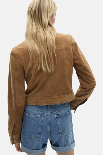 Blonde vrouw van achteren, bruin suède jasje, blauwe spijkerbroek.