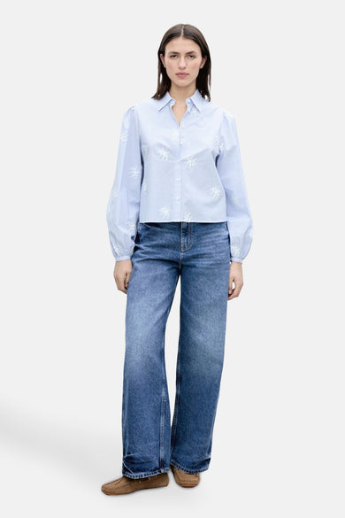 Chemise bleue rayée avec des manches longues de MANGO, avec des détails floraux blancs et associée à des jeans larges et des mocassins.
