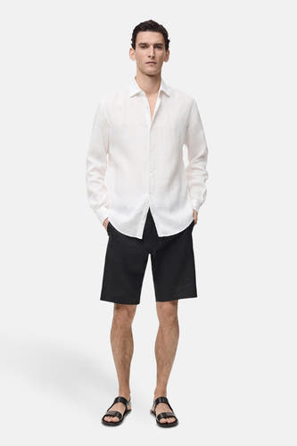 Short noir de MANGO, porté avec un chemisier blanc en lin et des sandales en cuir.