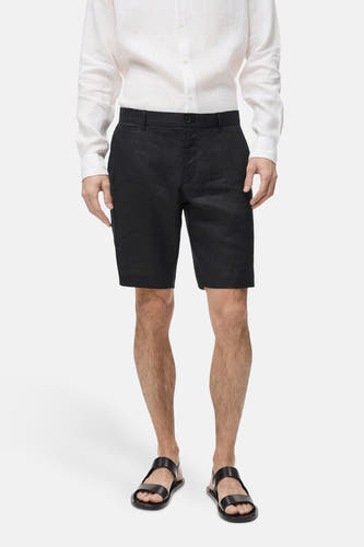 Short noir de MANGO, porté avec un chemisier blanc en lin et des sandales noires.