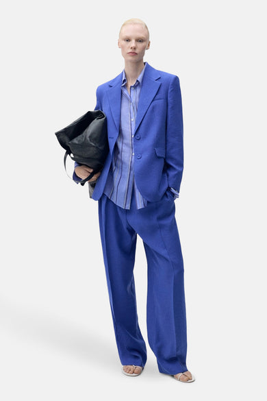Pantalon de costume bleu MANGO, avec des jambes larges et porté avec un chemisier rayé bleu et une sacoche noire.