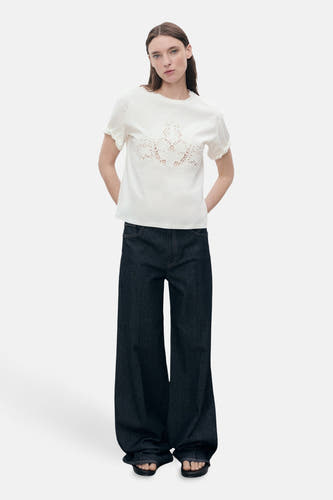 T-shirt blanc à manches courtes de MANGO, avec des détails de broderie élégants sur la poitrine et porté avec des jeans larges.