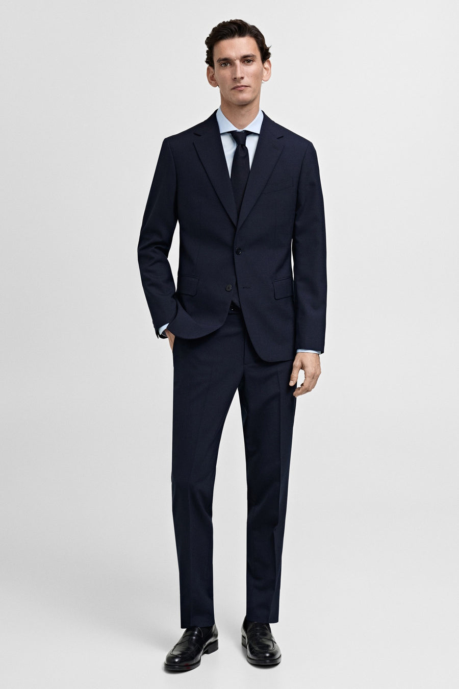 Chemise bleu clair à manches longues de MANGO, portée sous un costume bleu foncé avec une cravate assortie.